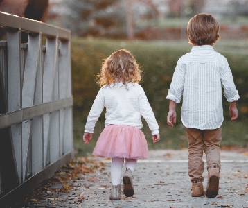 A young boy and his younger sister walk along a bridge with their backs to the camera