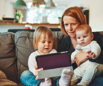 A mother with her two young children on her lap, all looking at a smart-tablet