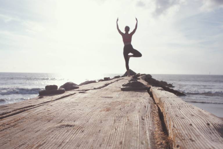 Man does tree pose in yoga on a rock at the beach