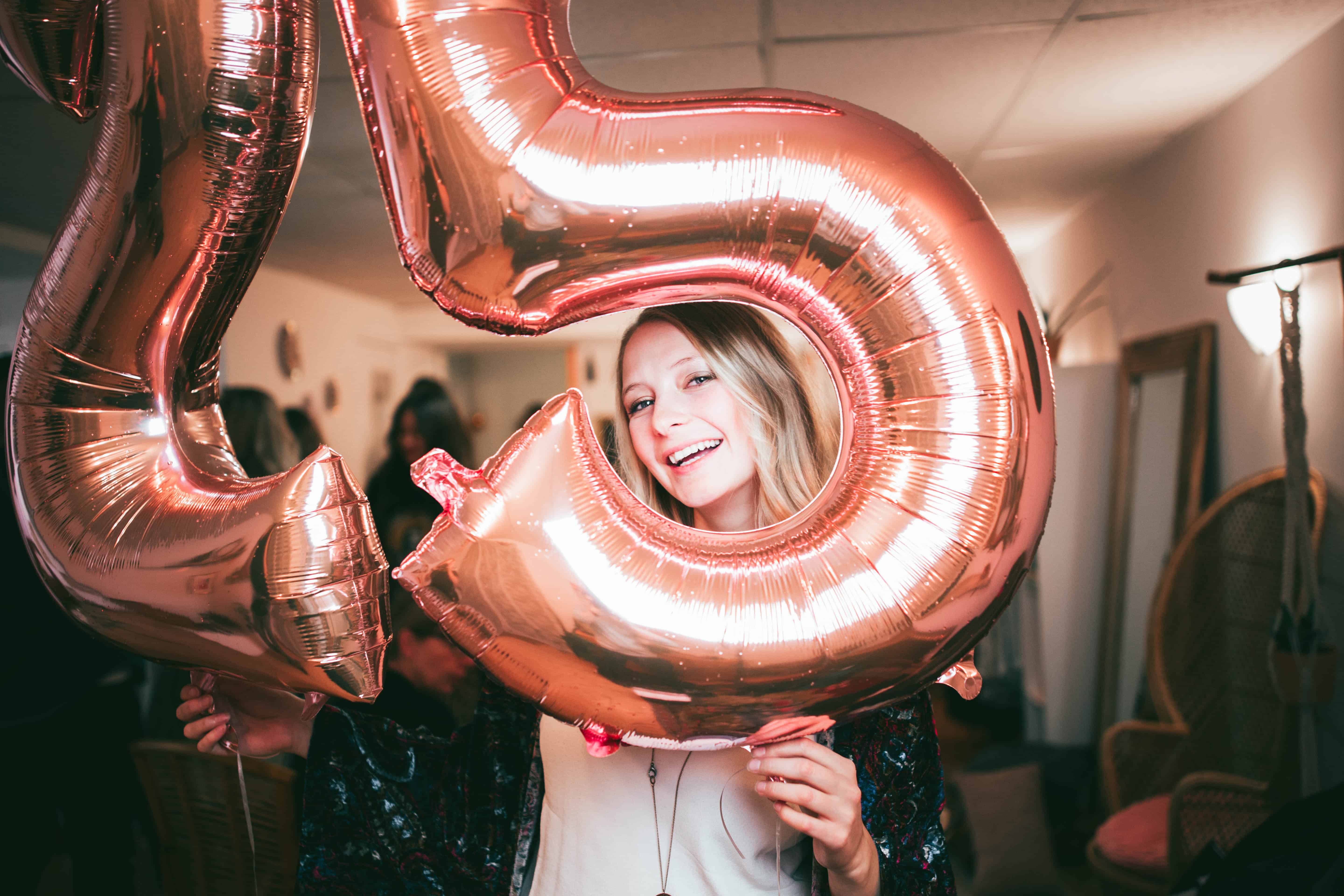 A happy woman smiles and holds birthday balloons with the number 25 on it