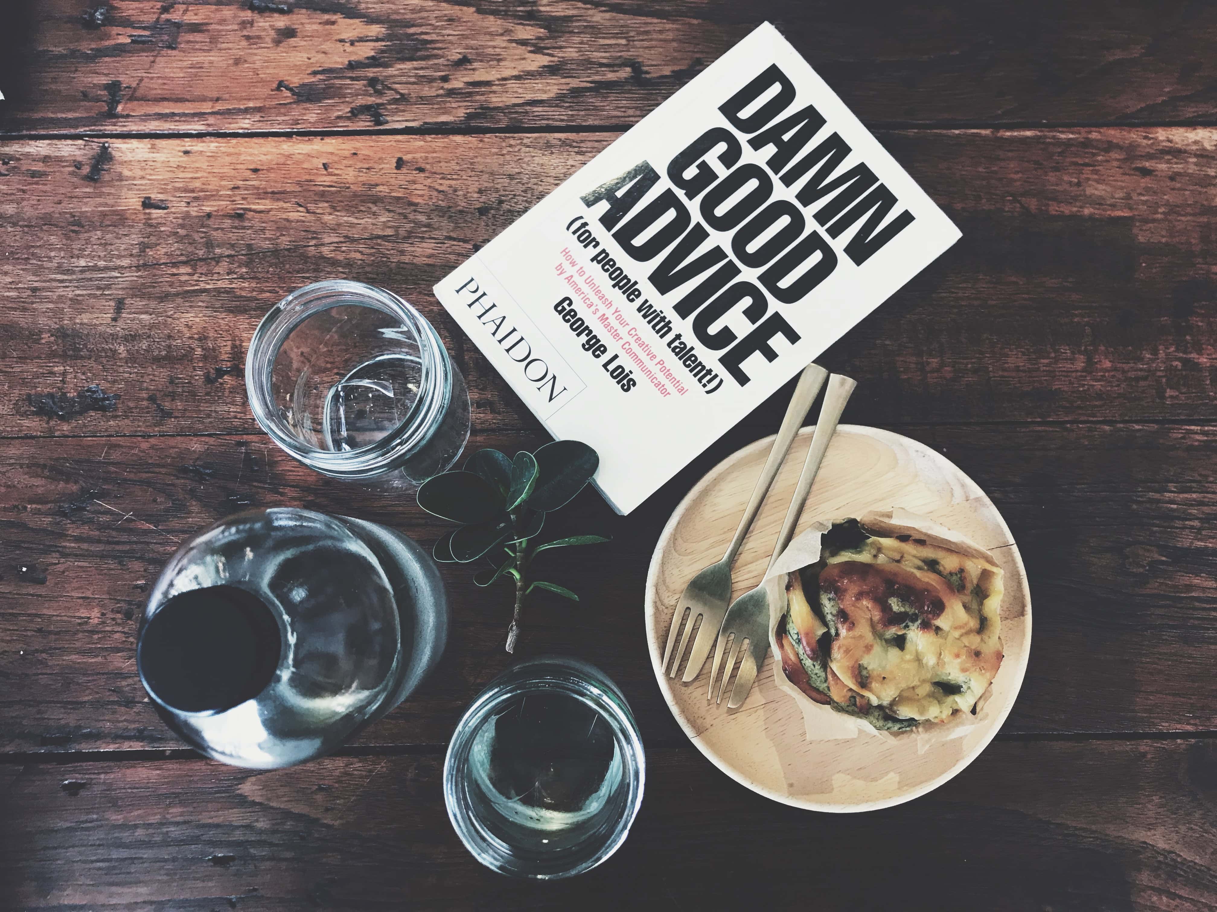Flat lay of a book with 'damn good advice' as the title next to food and water