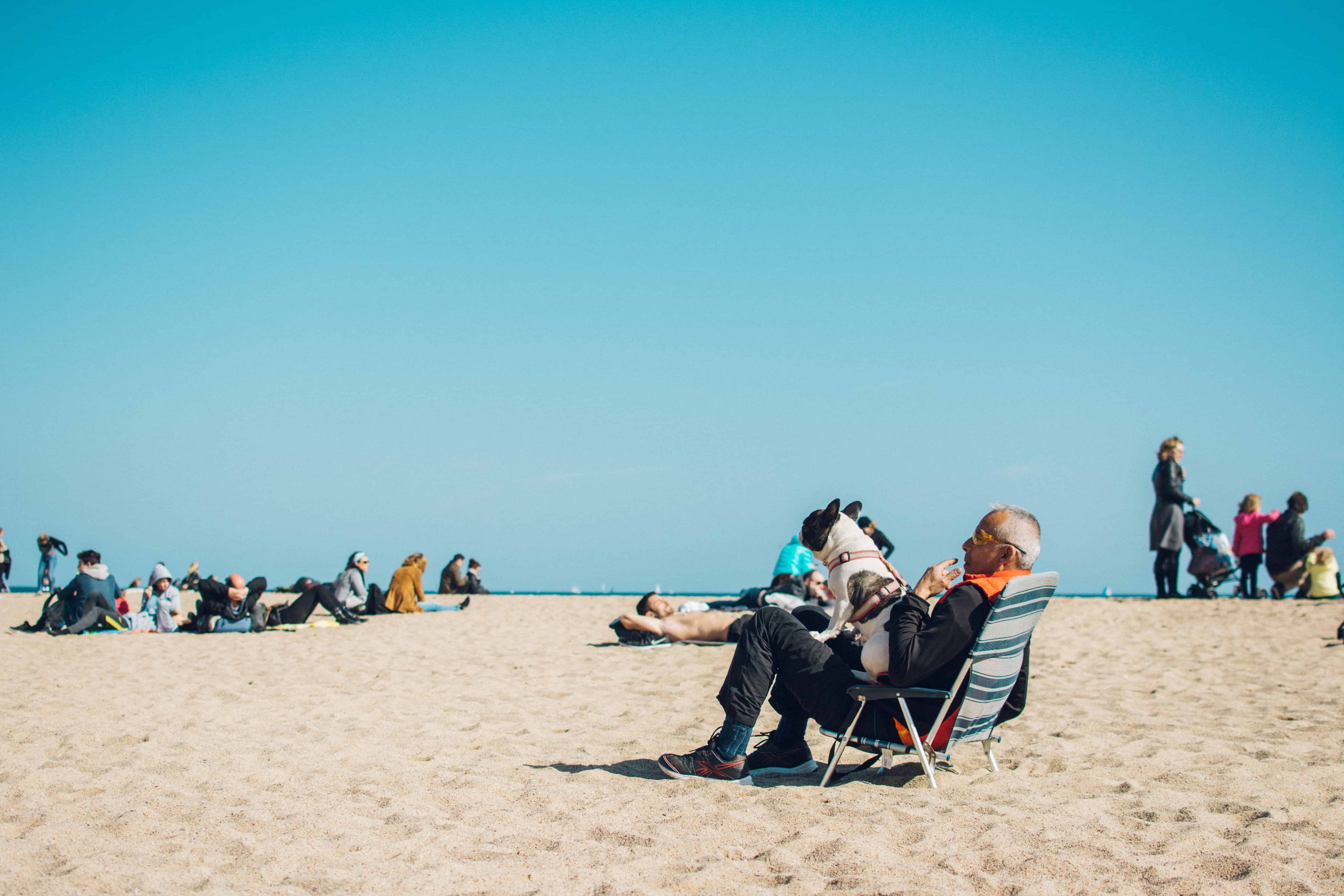 A man sits on a beach chair with his dog