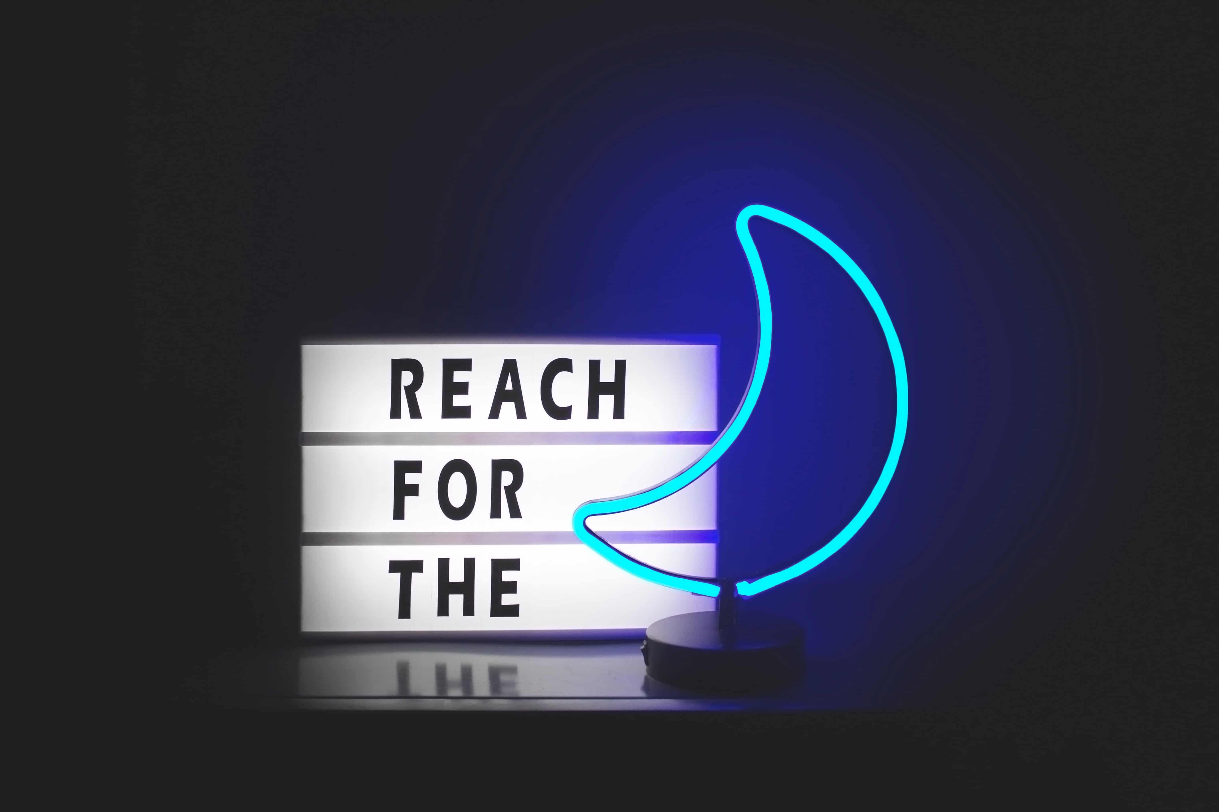 A neon blue moon next to a sign that says 'reach for the'