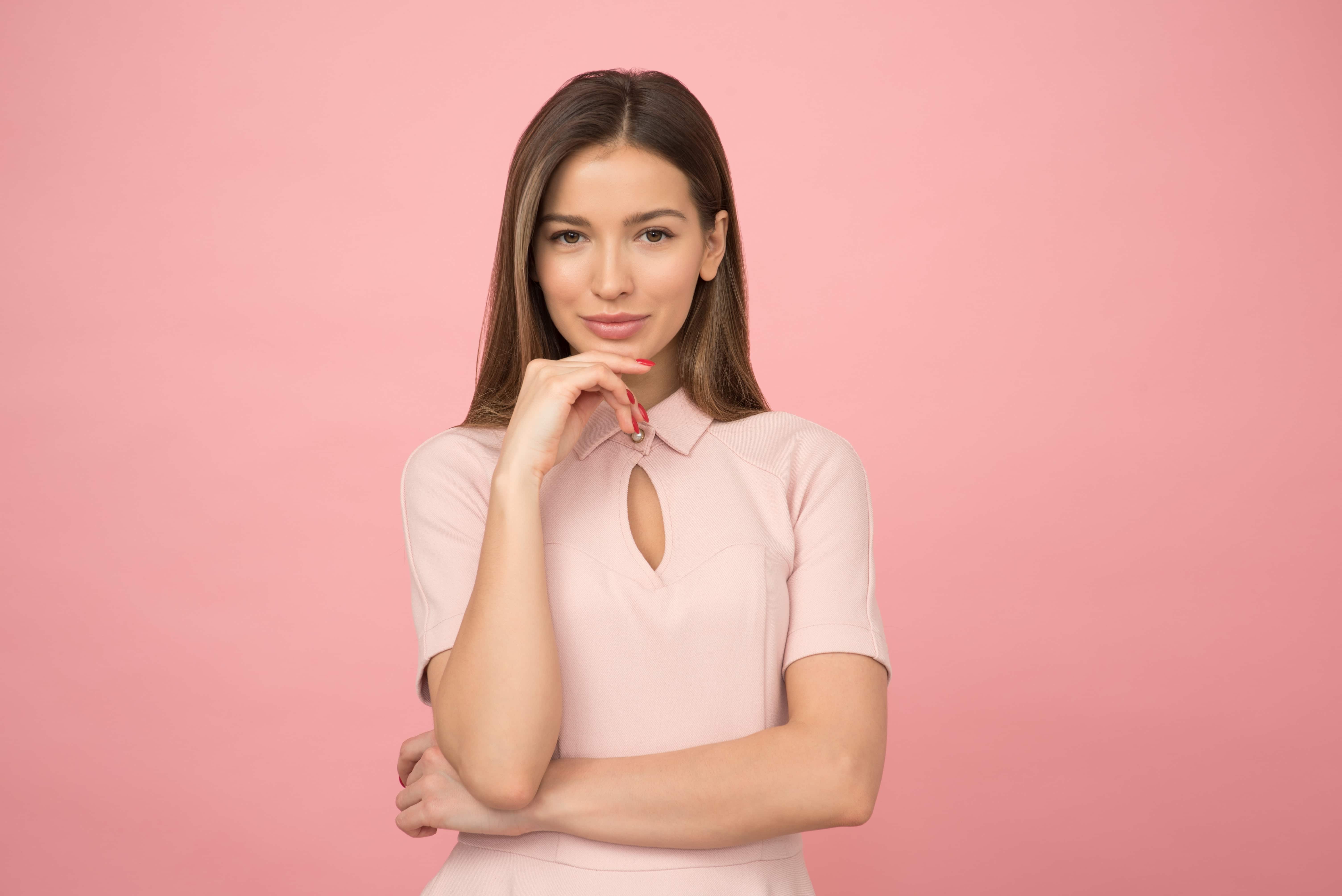 A professional woman stands against a pink background